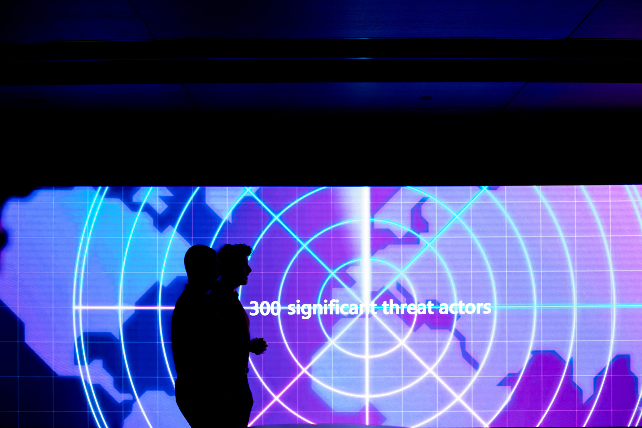 Two silhouettes walk past a large LED Screen